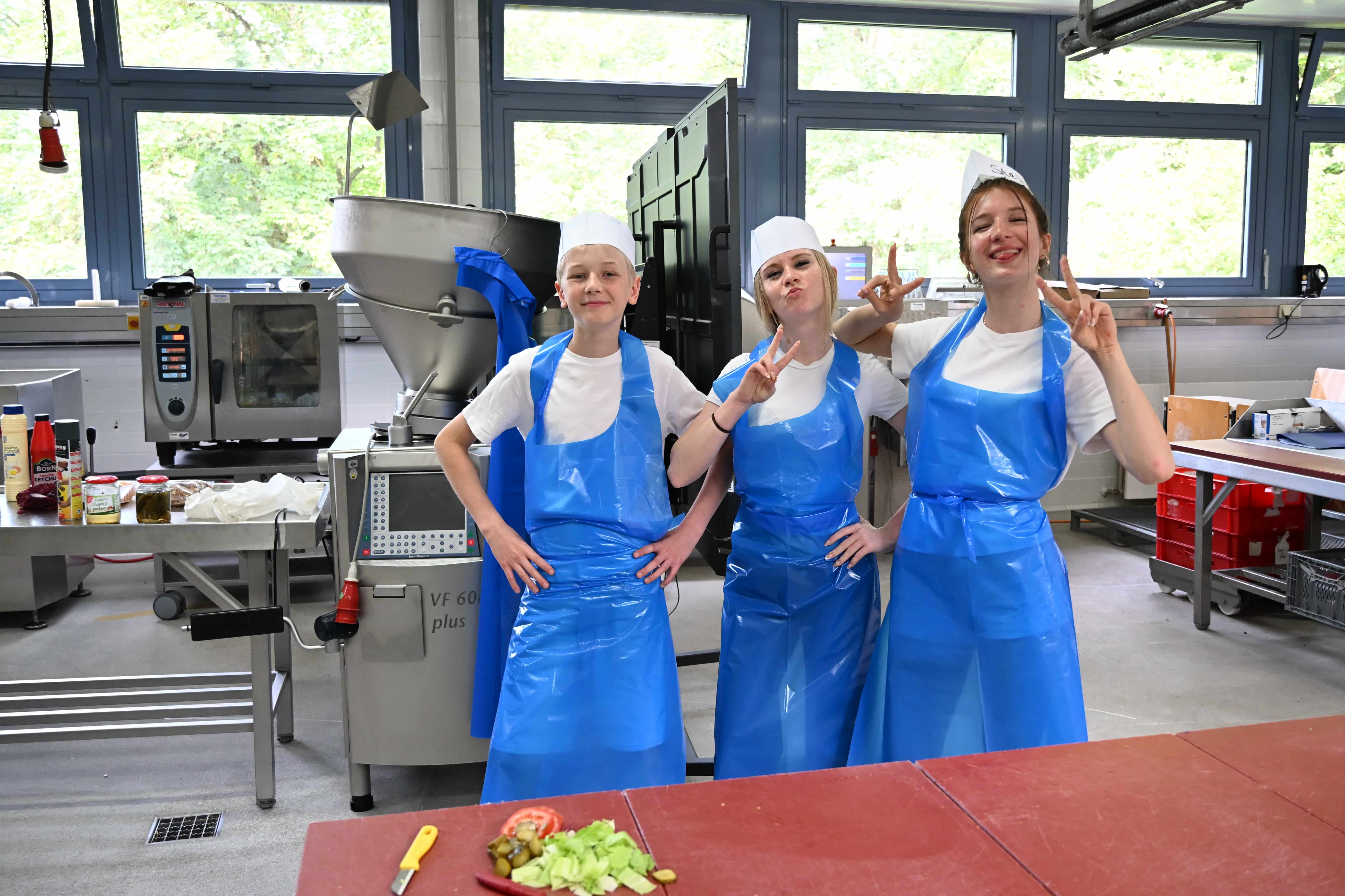 Drei fröhliche Personen in blauen Schürzen zeigen Peacezeichen in Küche