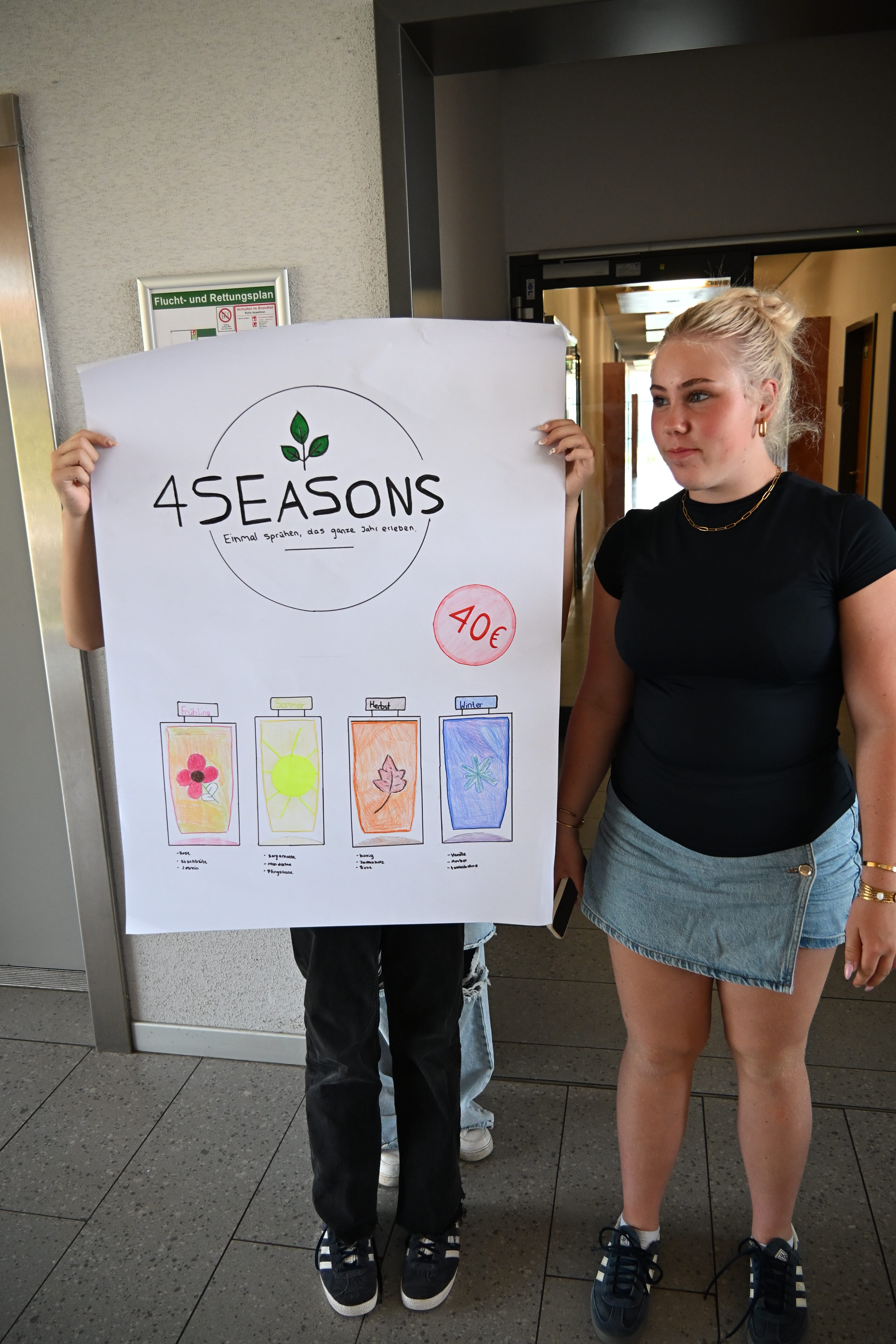 Junge Frau ernst neben Plakat 4SEASONS bunt und 40 Euro Markierung