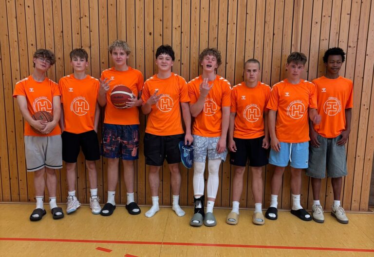 Acht Jugendliche in orangefarbenen Trikots, neutral, vor Holzwand, ein Beinprothese