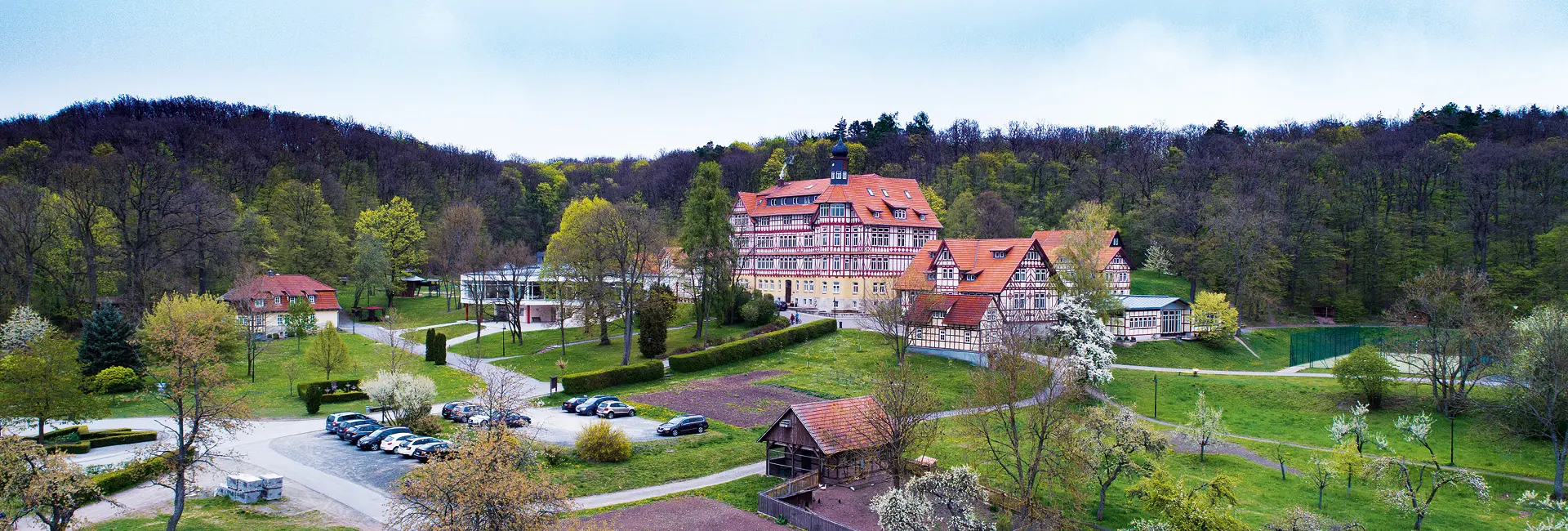 Heiteres Schloss mit roten Daechern in gruener Parklandschaft und Wald