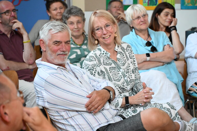 Laechelndes blondes Paar in Weiss und Gruen mit Brille im Publikum