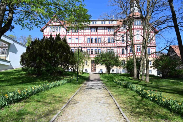 Historisches Fachwerkgebaeude in Rot und Weiss mit Weg und bluehendem Garten