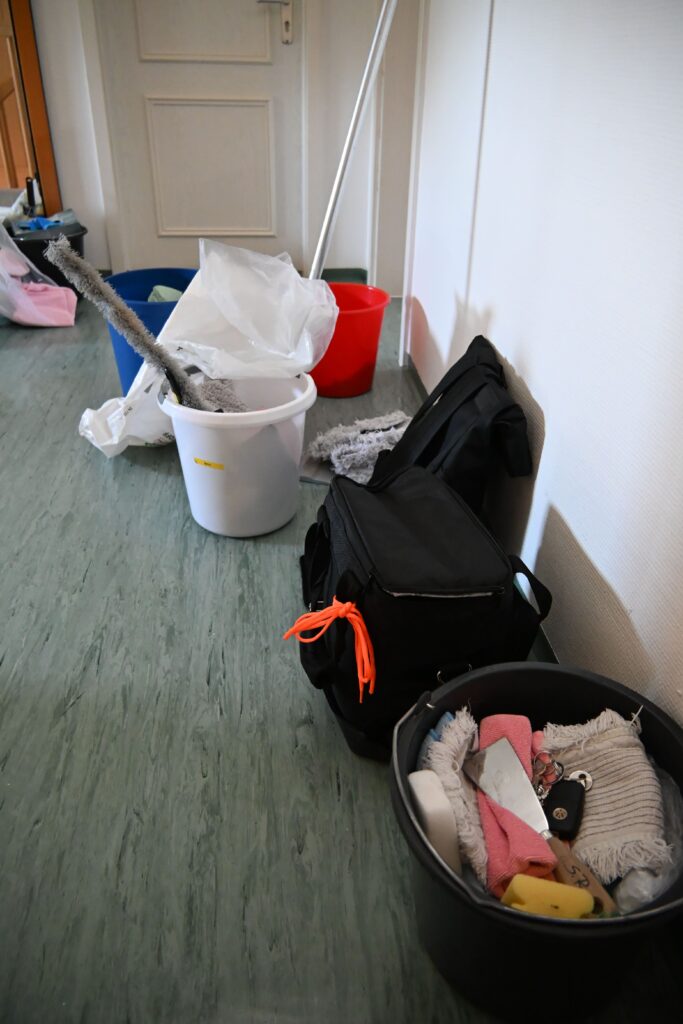 Reinigungsutensilien mit schwarzer Tasche Eimern und Moppen an gruener Wand