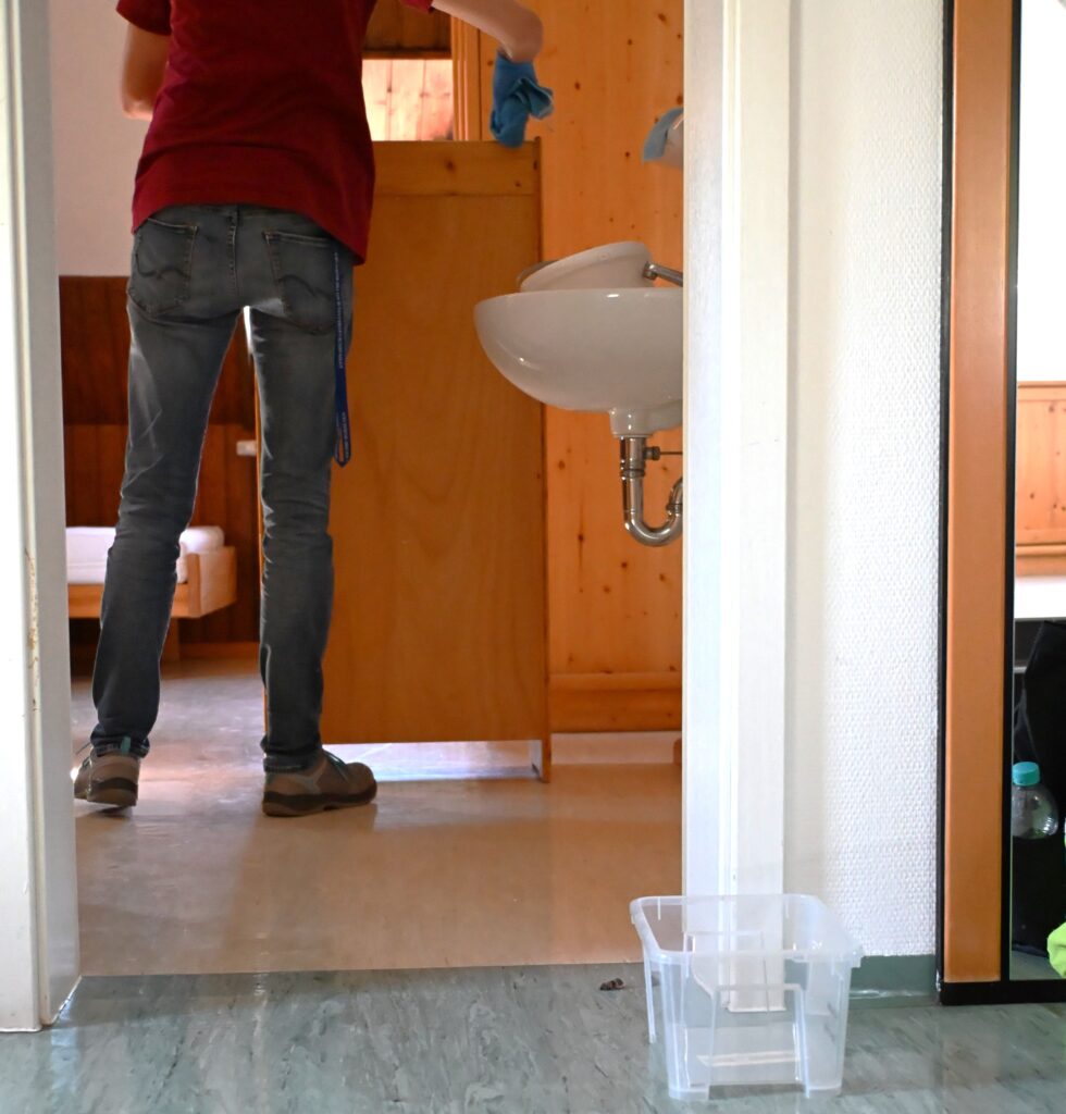 Eine Person im roten Shirt und in Jeans putzt mit einem blauen Tuch