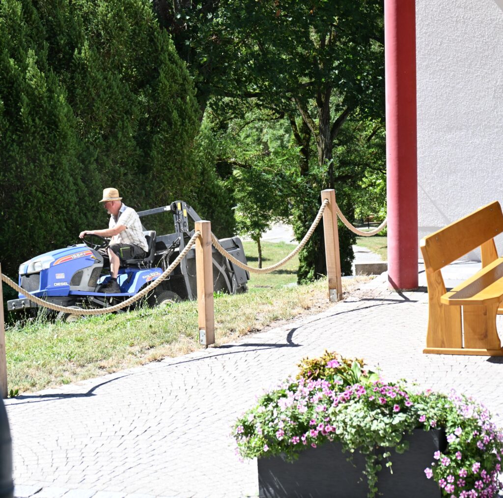 Ein Mann mit Strohhut faehrt einen blauen Aufsitzmaeher im gruenen Park