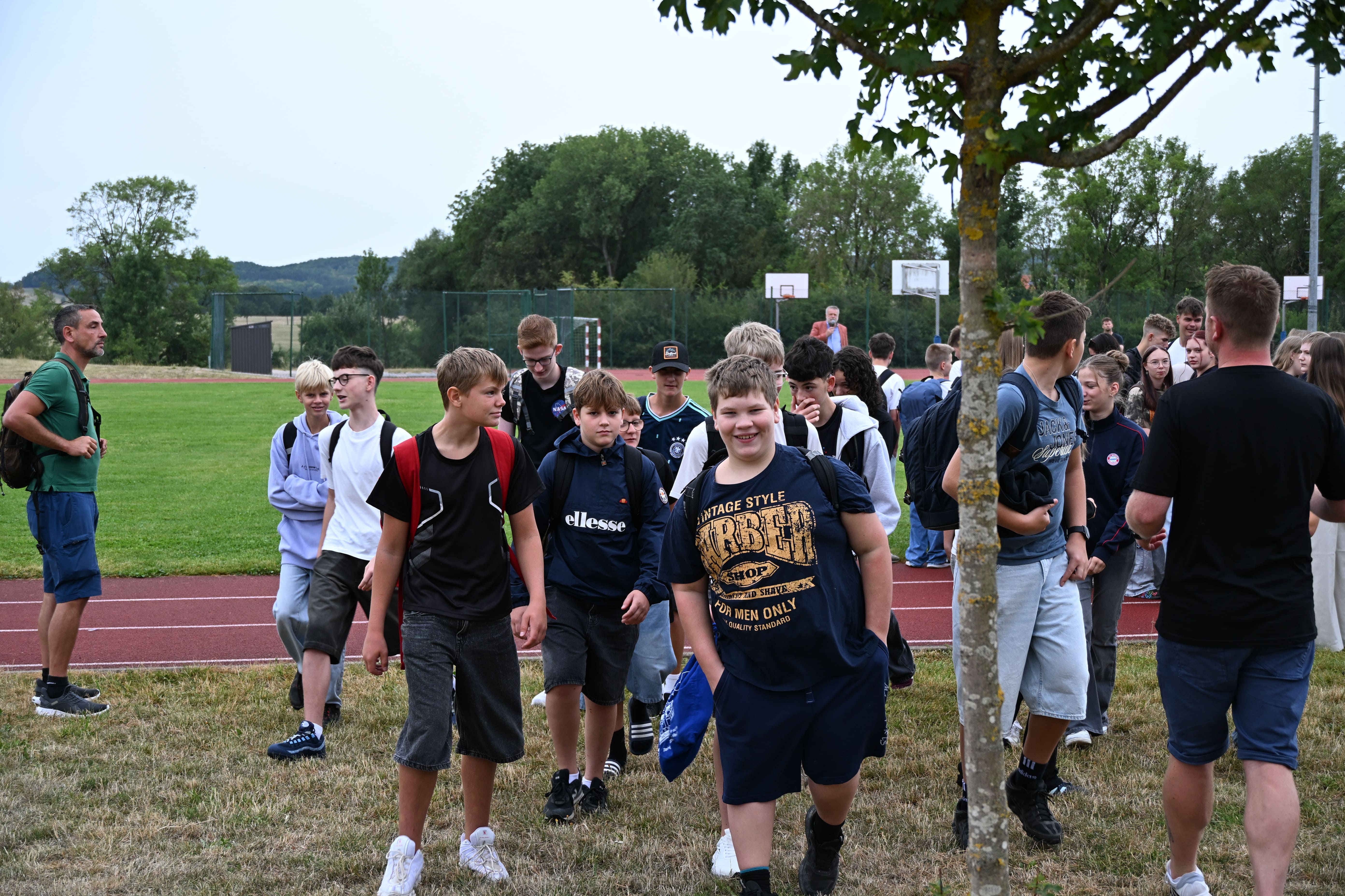 Eine Gruppe froehlicher Jugendlicher mit Rucksaecken auf einem Sportplatz