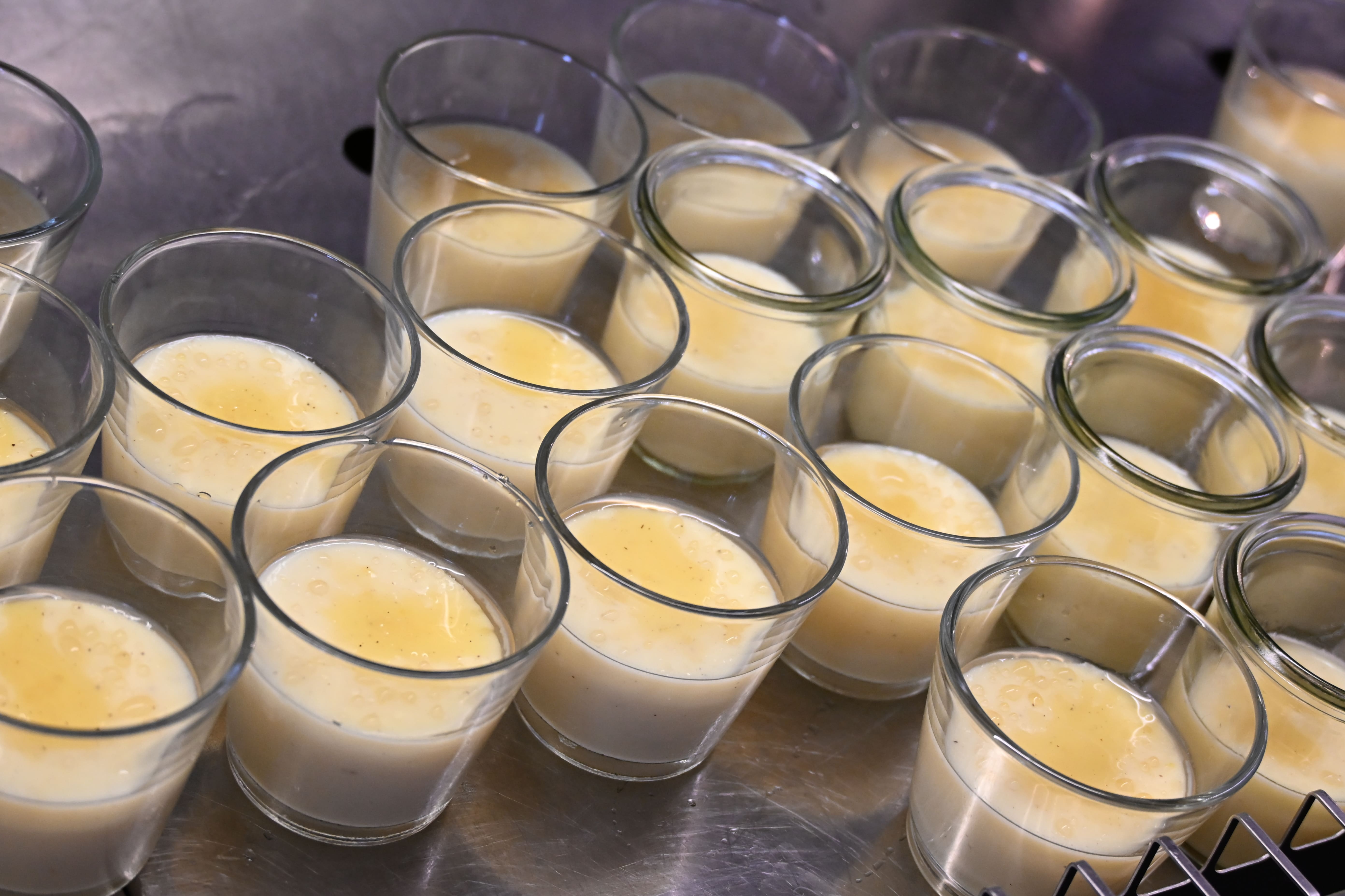 Mehrere Glaeser mit cremigem gelblichem Vanillepudding auf einer Metallflaeche