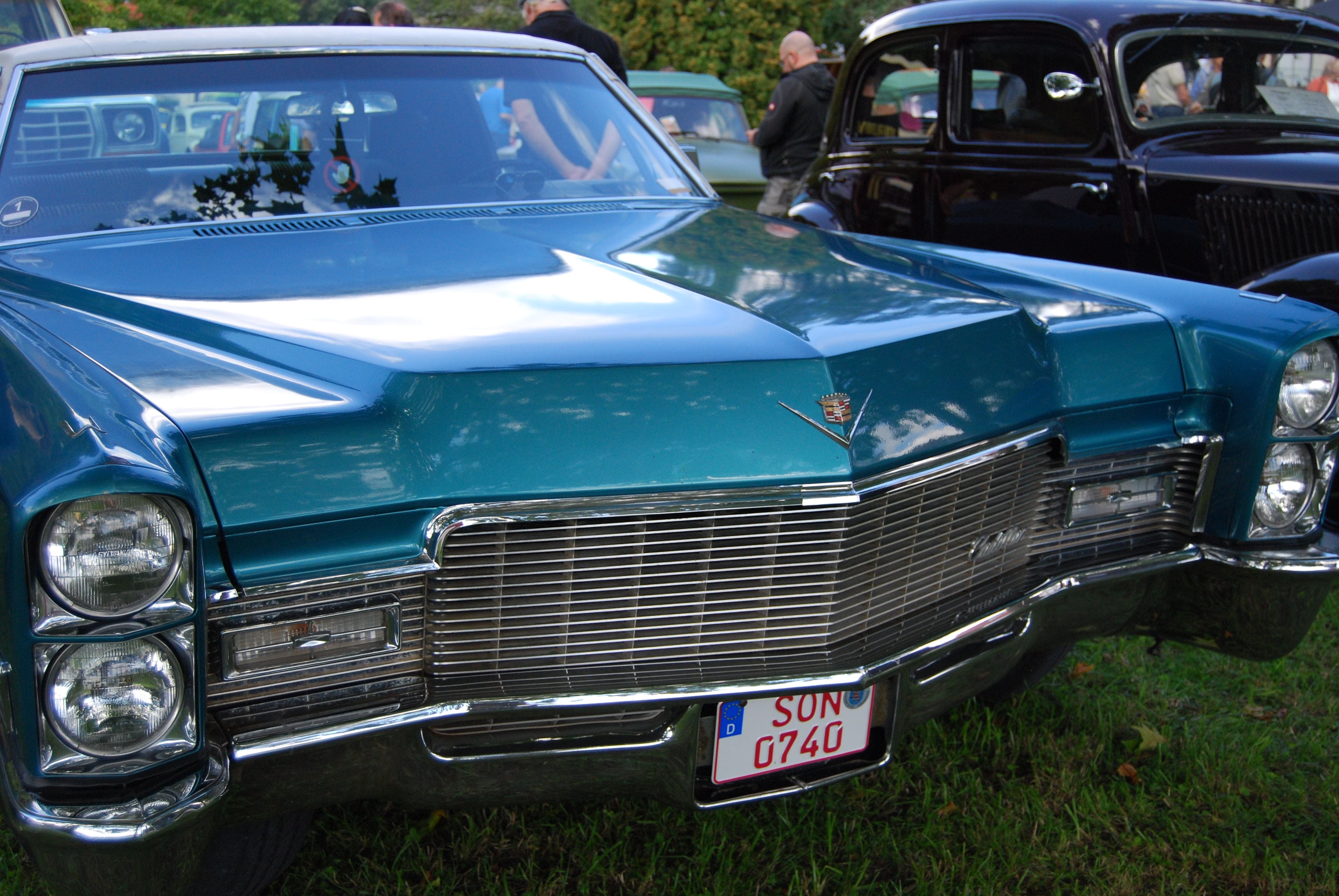 Ein tuerkisfarbener Cadillac Oldtimer mit glaenzendem Chromgrill auf einer Wiese