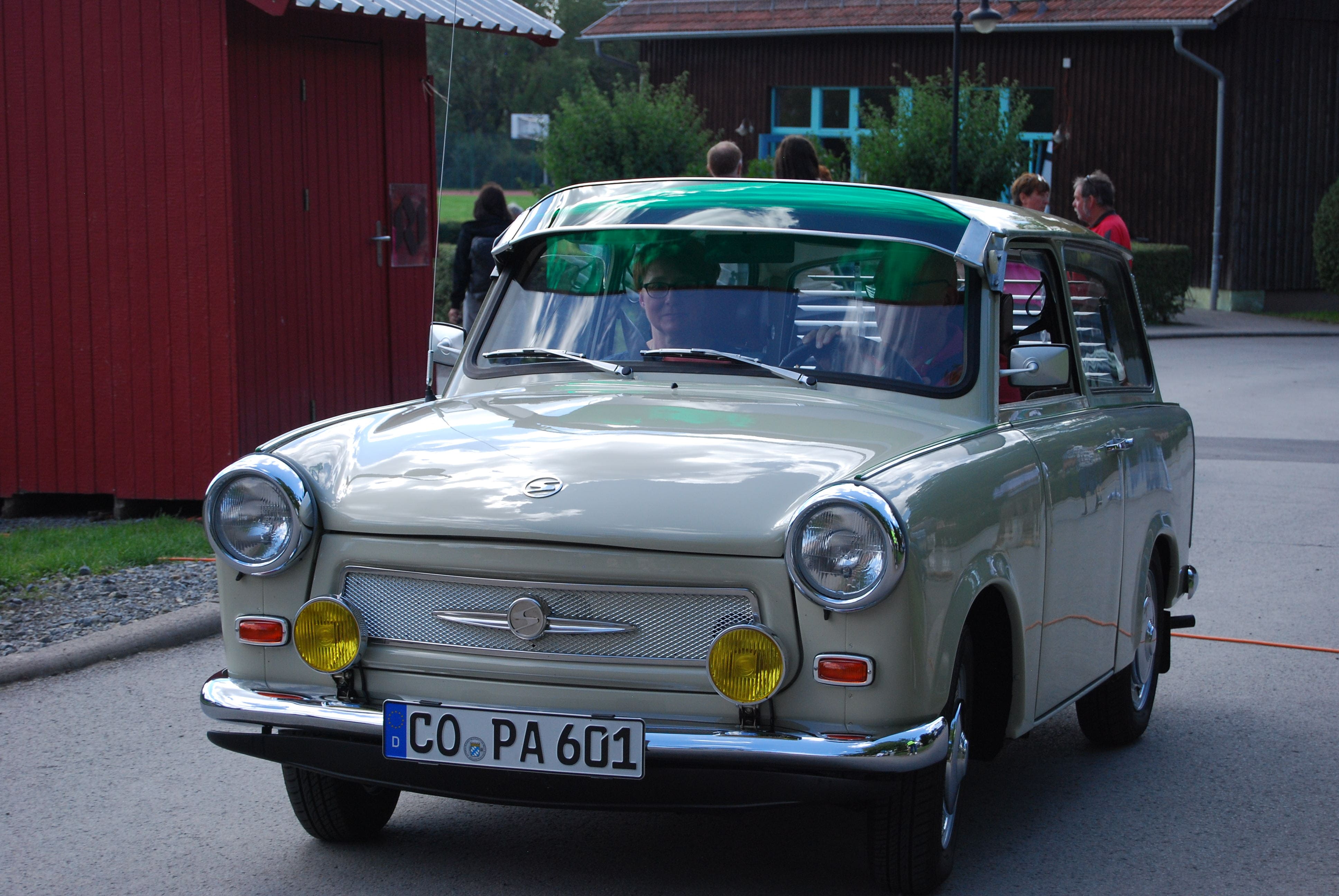 Frau mit Brille faehrt einen cremefarbenen Oldtimer mit gelben Scheinwerfern