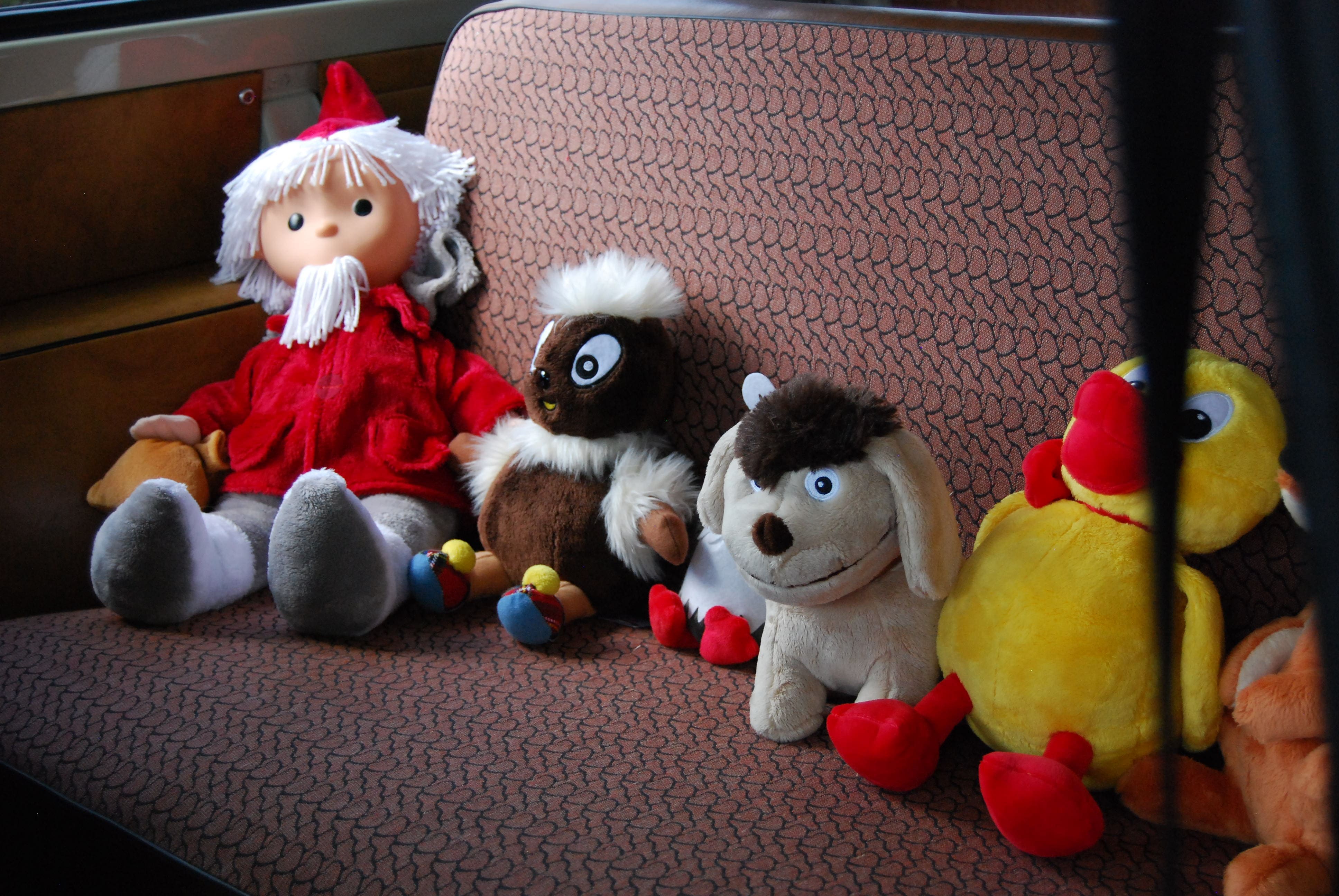 Bunte Kuscheltiere und eine Puppe mit rotem Mantel sitzen auf einer Bank