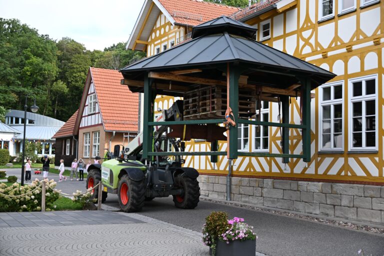 Ein gruener Teleskoplader hebt einen Pavillon vor gelbem Fachwerkhaus