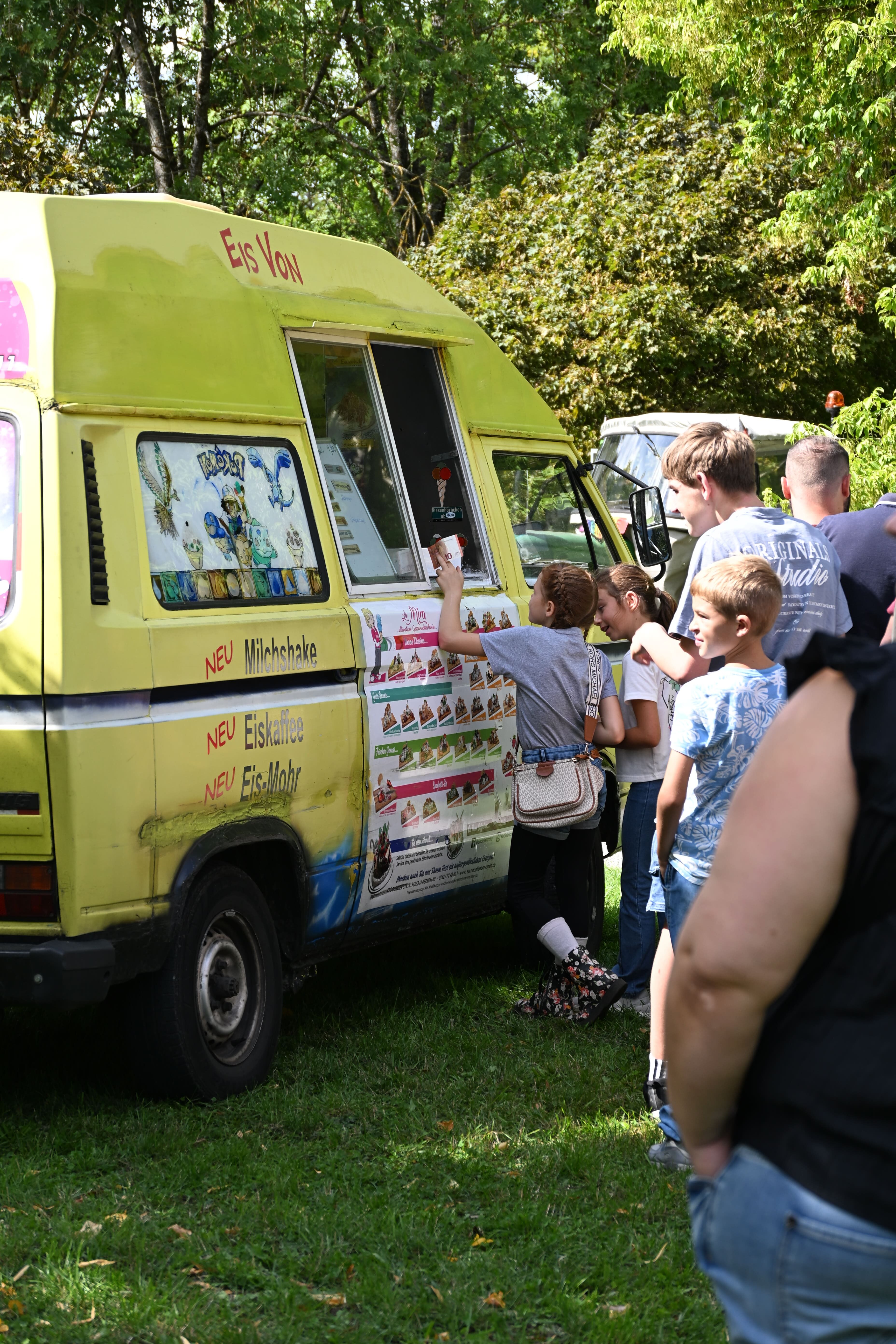 Menschen stehen an einem gelben Eiswagen und kaufen Eis im Freien