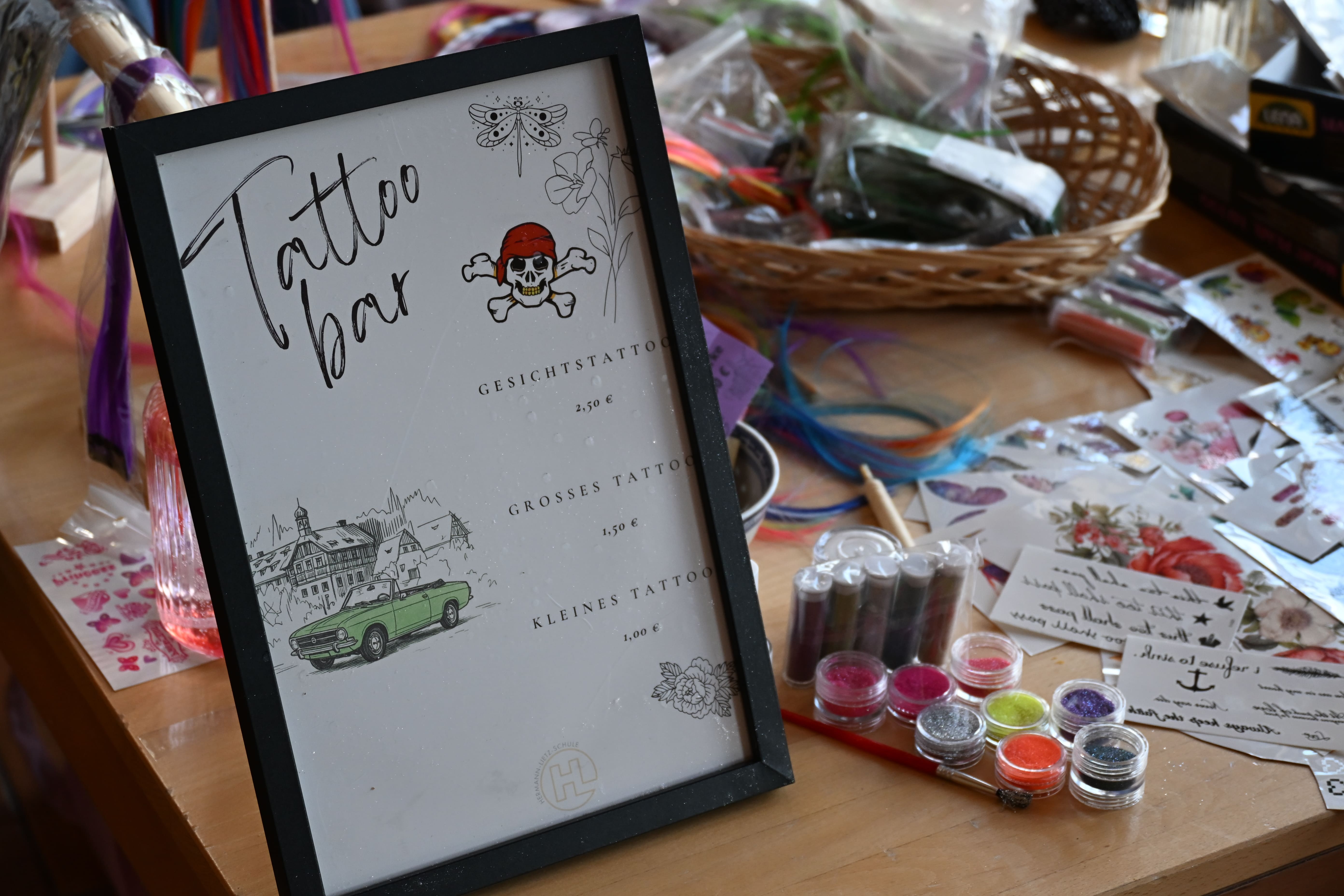 Schild mit Aufschrift Tattoo Bar neben buntem Glitzer und Klebetattoos auf Tisch