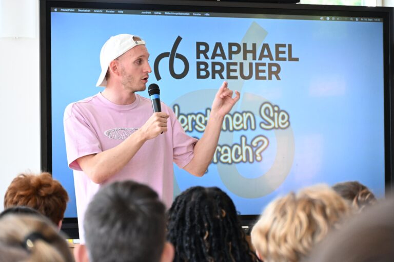 Ein junger Mann mit weisser Kappe und rosa Shirt spricht engagiert ins Mikrofon