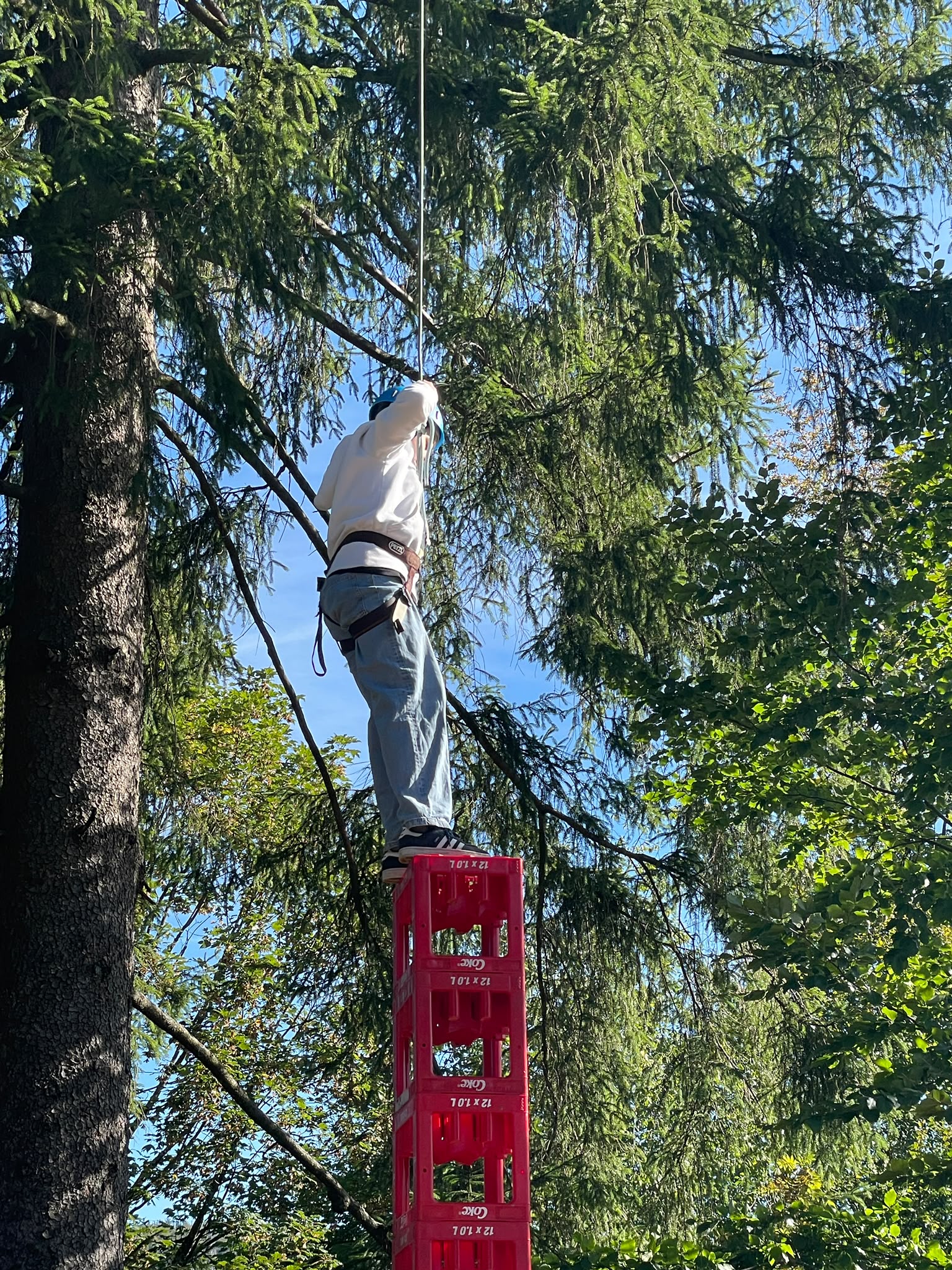 Person mit Helm und Klettergurt balanciert konzentriert auf roten Getraenkekisten