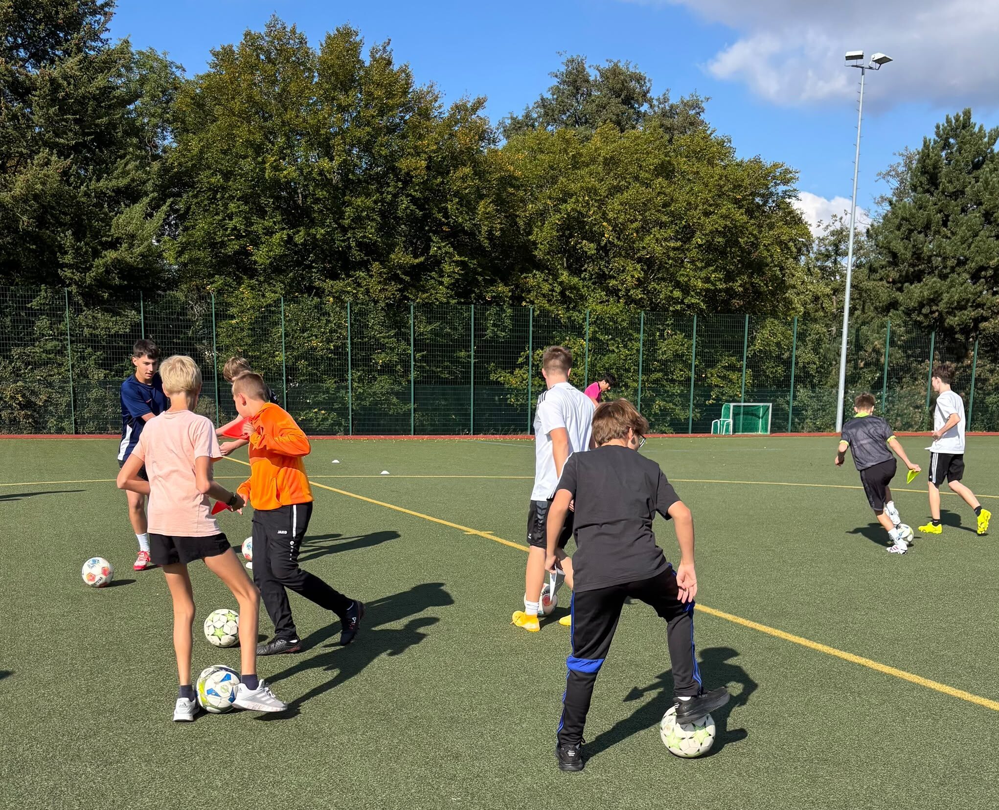 Jugendliche Fussballspieler trainieren konzentriert mit Baellen auf einem Kunstrasenplatz