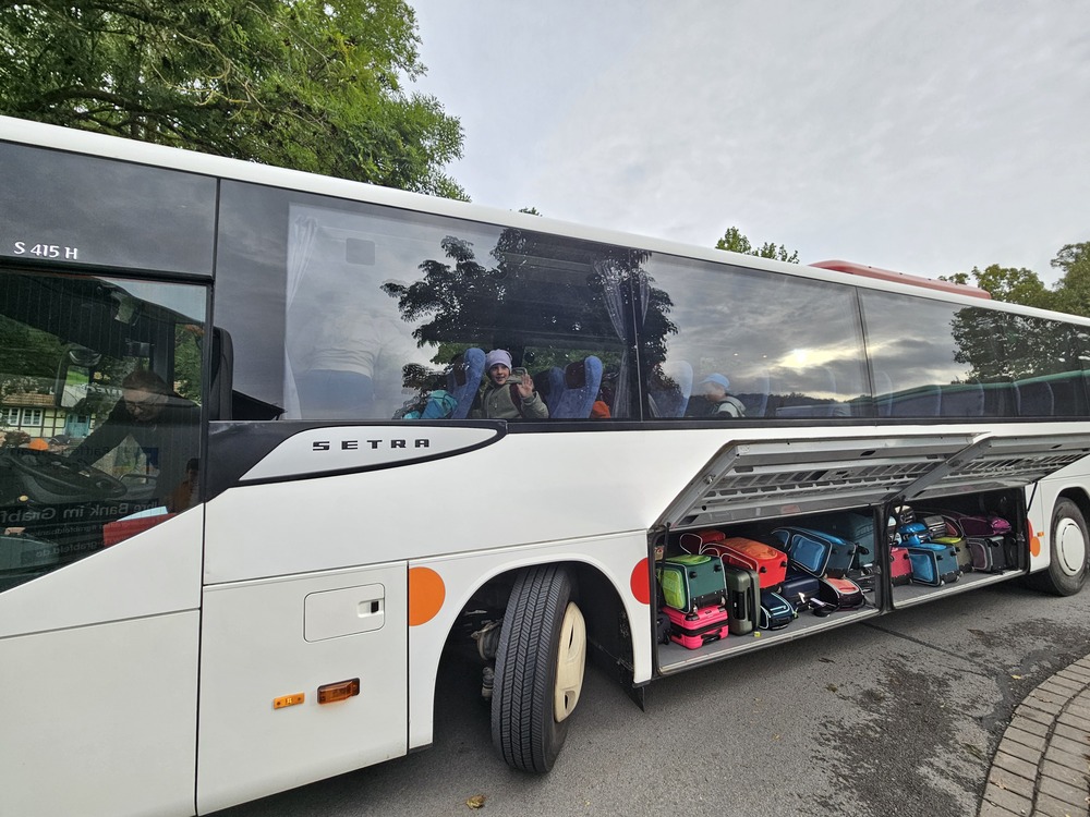 Weisser Setra Reisebus mit winkendem Kind am Fenster und bunten Koffern