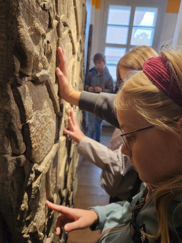 Ein neugieriges blondes Maedchen mit Brille ertastet eine Steinmauer