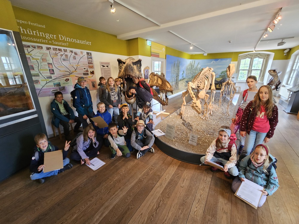 Froehliche Kindergruppe im Dinosauriermuseum vor einem Skelett in Thueringen