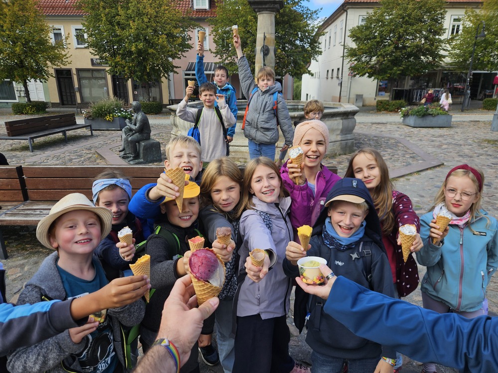 Froehliche Kinder strecken auf einem Platz laechelnd ihr Eis in die Hoehe