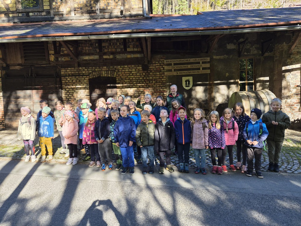 Eine Gruppe laechelnder Kinder mit einem Erwachsenen vor einem alten Museum