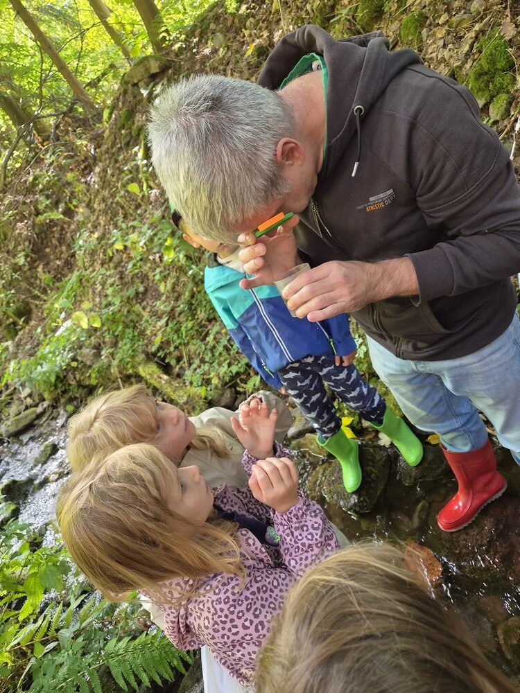 Ein Mann mit grauem Haar untersucht konzentriert etwas mit Kindern im Wald