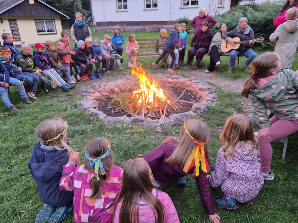 Kinder und Erwachsene sitzen um ein loderndes Lagerfeuer im Freien