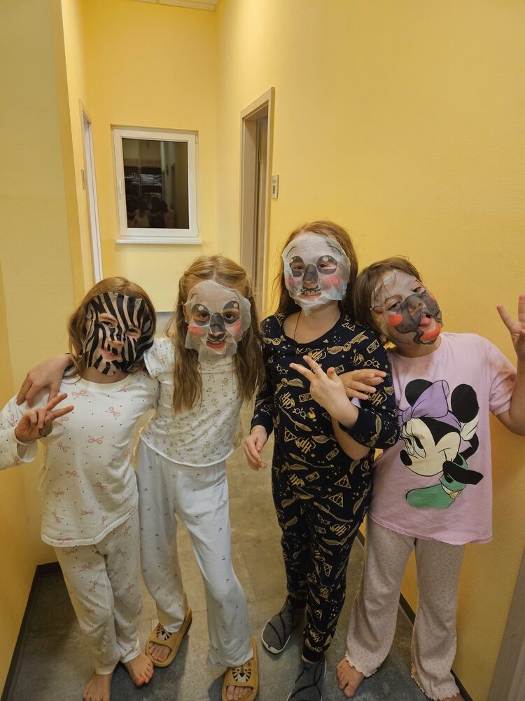 Vier froehliche Kinder in Pyjamas mit lustigen Tiergesichtsmasken im gelben Flur