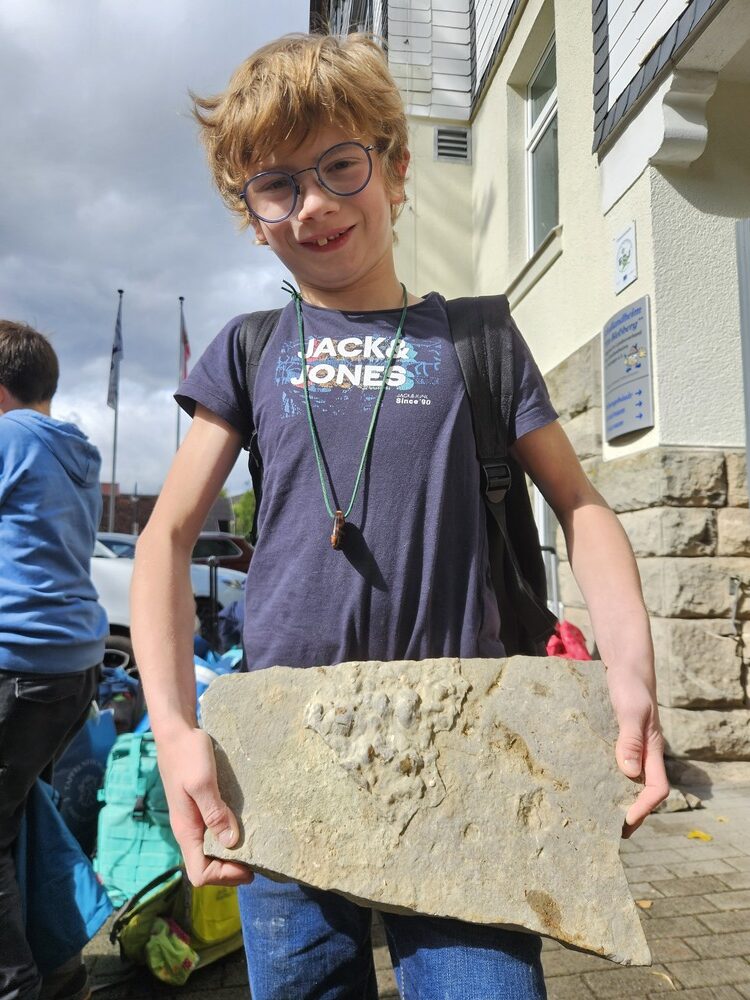 Laechelnder Junge mit Brille und blauem Shirt haelt eine grosse Steinplatte