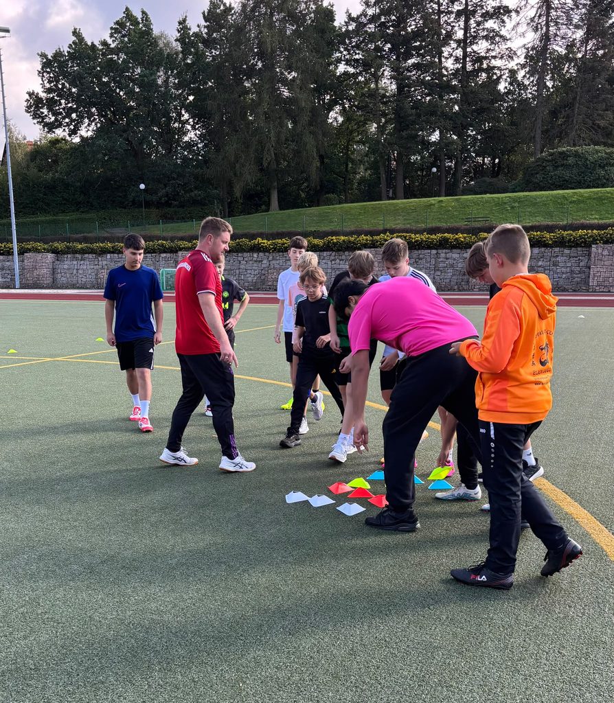 Ein Trainer in Rot leitet Jugendliche beim Fussballtraining mit bunten Huetchen an