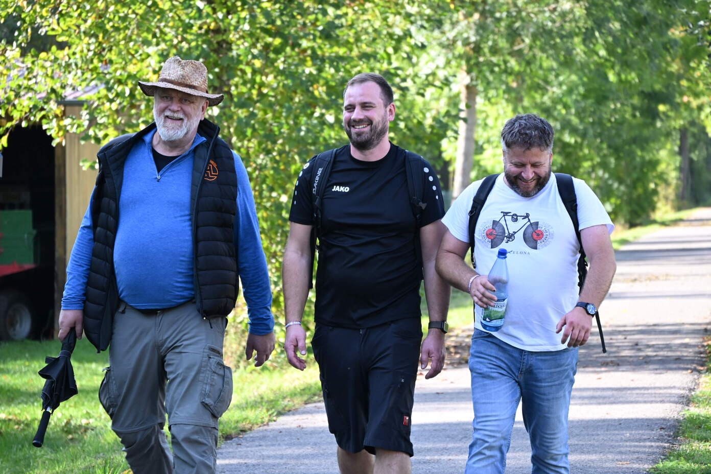 Drei laechelnde Maenner spazieren gut gelaunt auf einem Weg durch gruene Natur