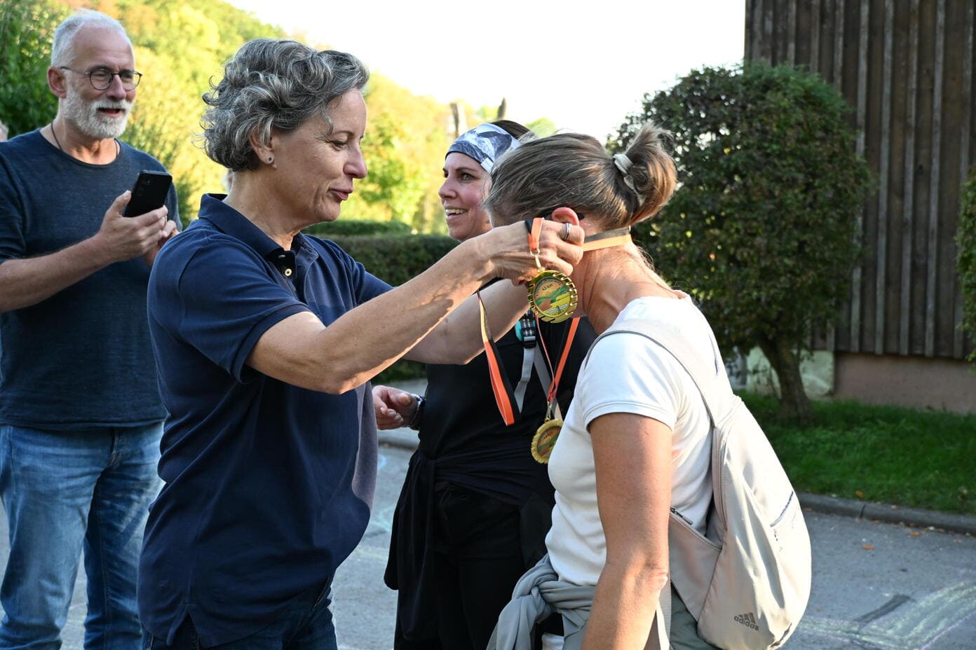 Eine laechelnde Frau legt einer Sportlerin stolz eine goldene Medaille um