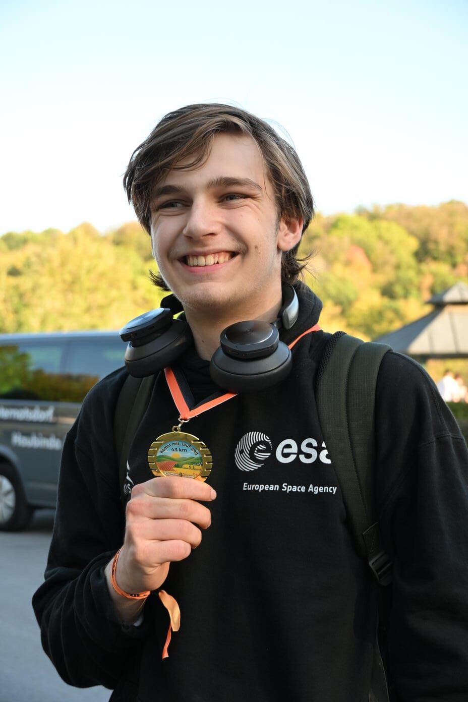 Laechelnder junger Mann im schwarzen ESA Pullover zeigt stolz eine Medaille
