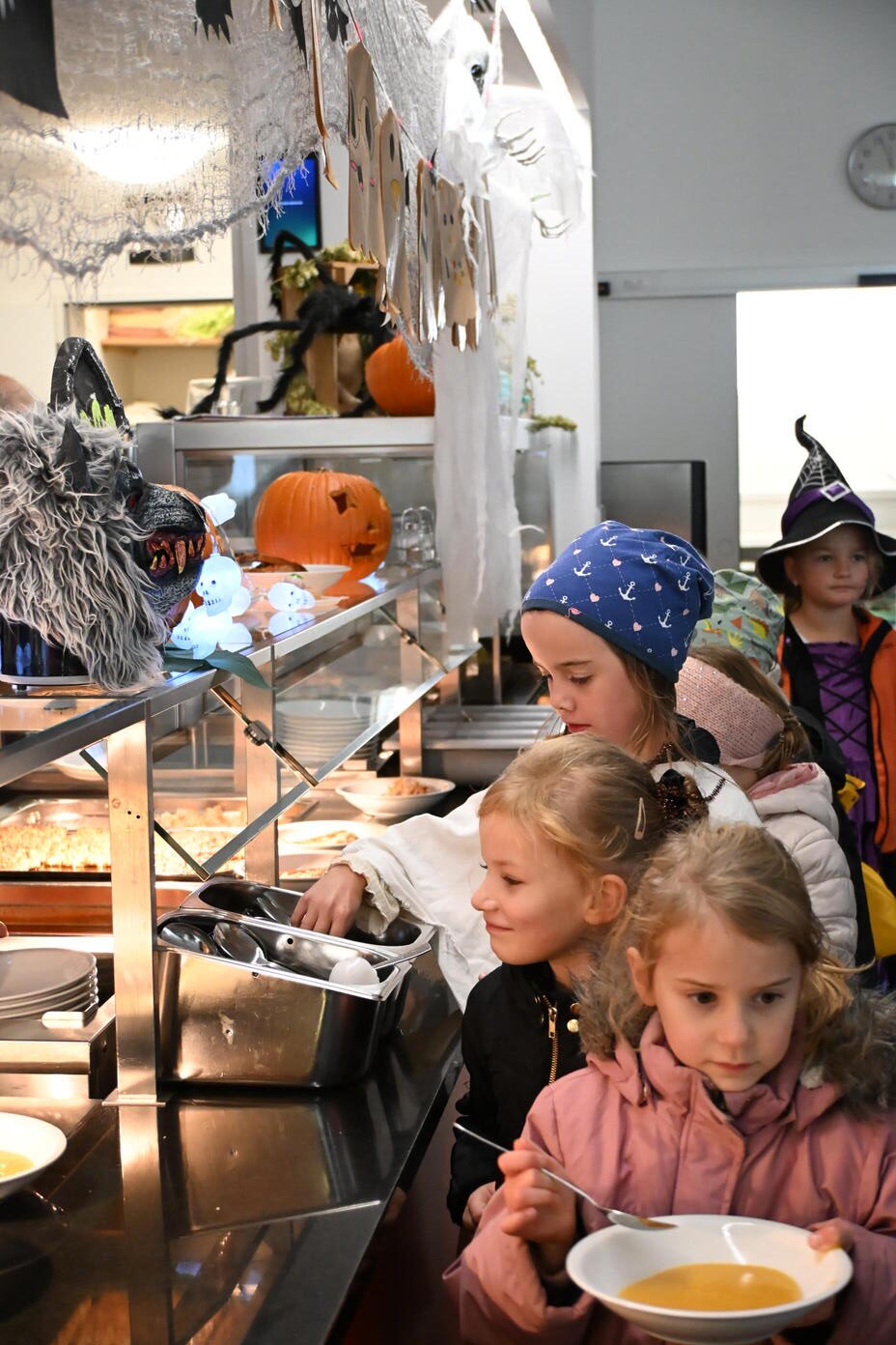Kinder in Kostuemen stehen an einem Halloween Buffet mit Kuerbis und Suppe