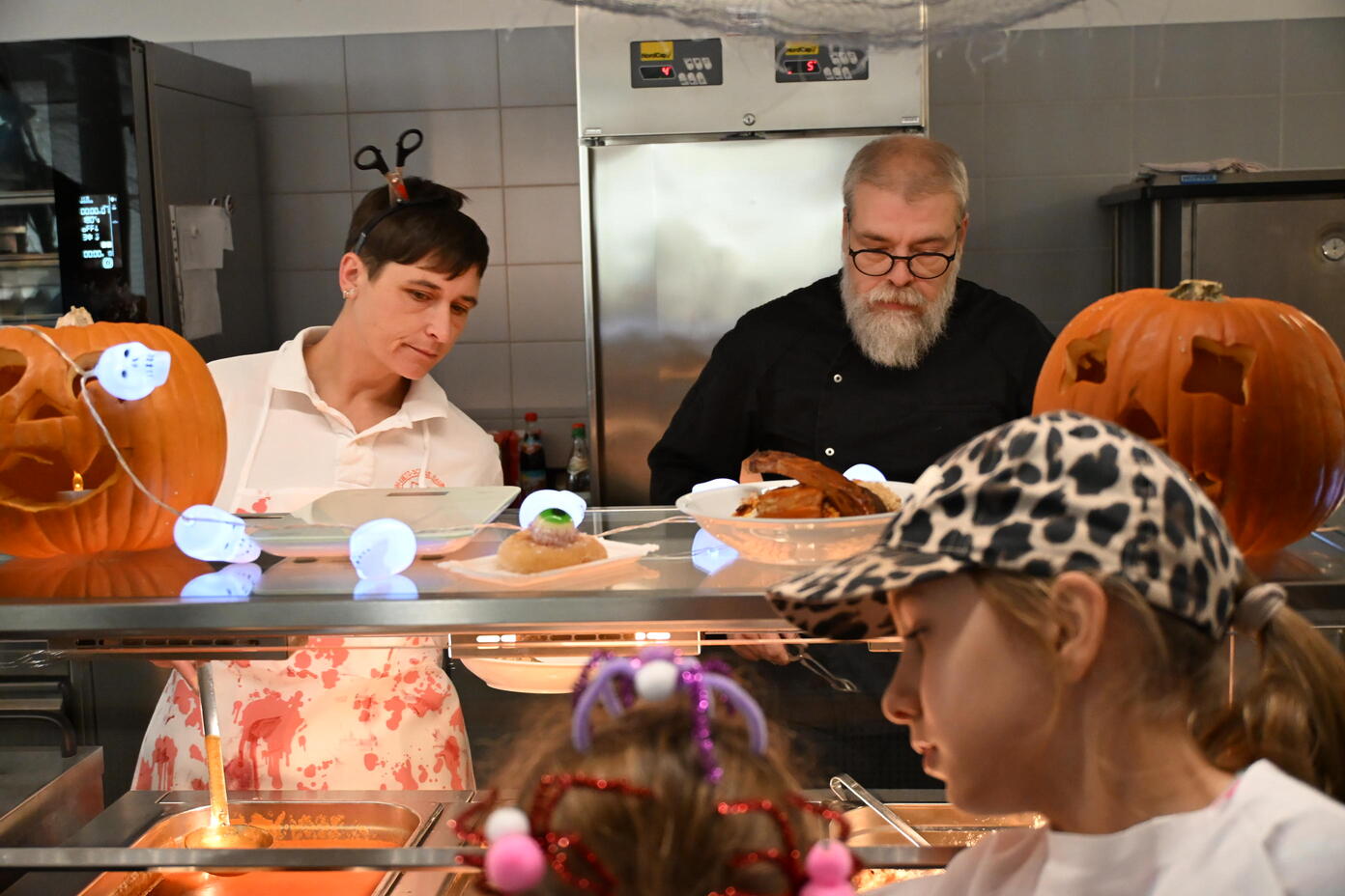 Erwachsene servieren Kindern Essen an einer Halloween dekorierten Theke