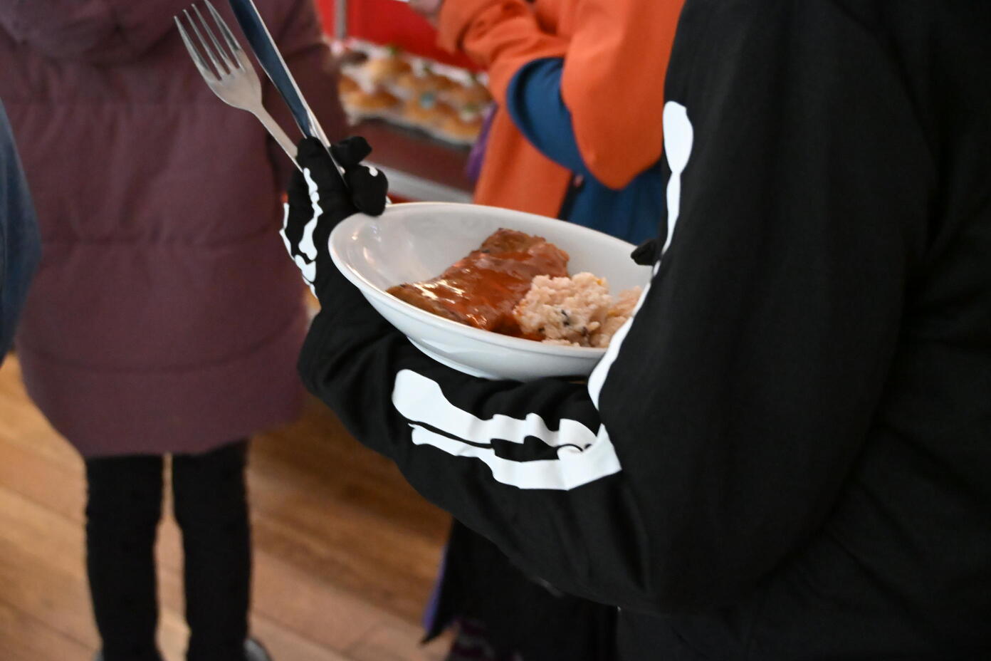 Person im Skelettkostuem haelt Schale mit Fleisch und Reis sowie eine Gabel