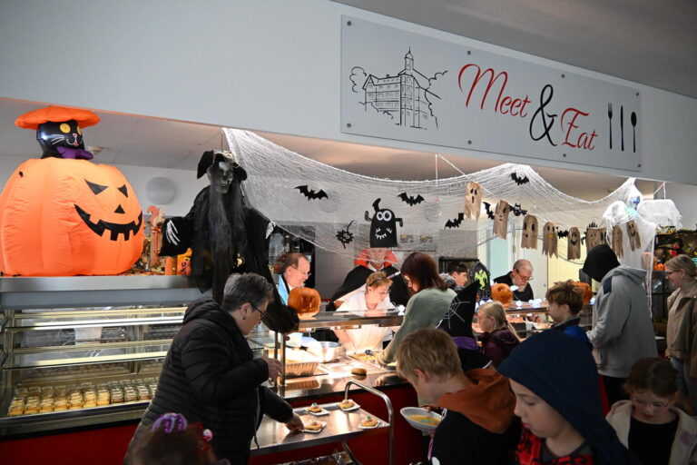 Menschen an einer Halloween Essensausgabe mit Kuerbis und Geister Deko