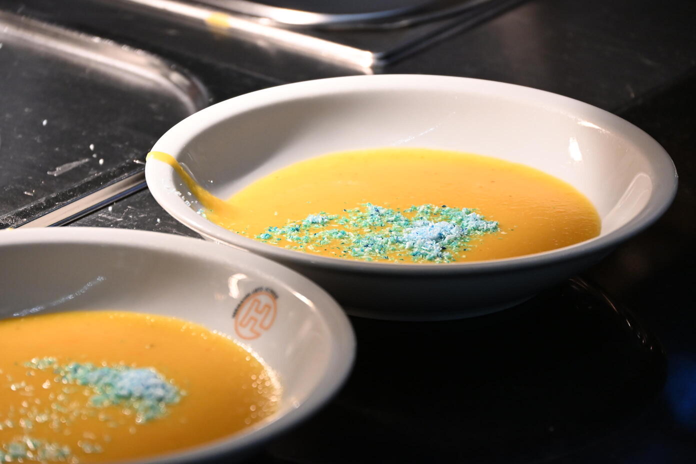Zwei weisse Schalen mit orangefarbener Suppe und blaugruener Garnierung