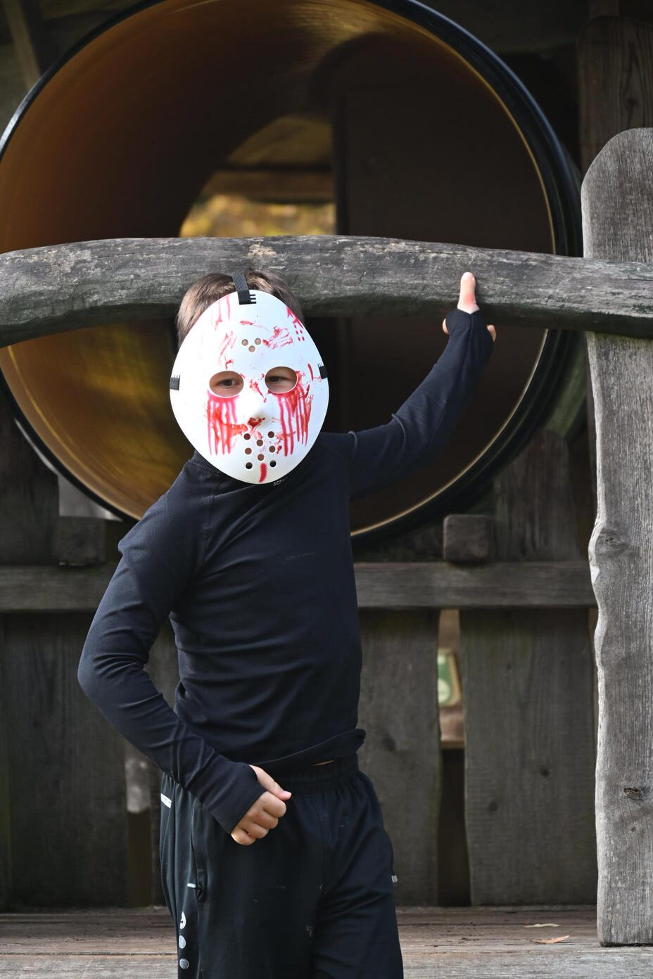 Ein Kind in schwarzer Kleidung traegt eine weisse Hockeymaske mit Blut