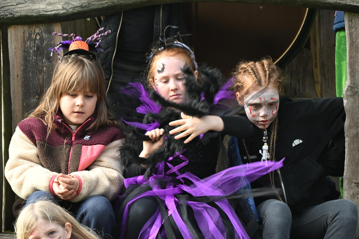 Drei Kinder in Halloween Kostuemen mit Schminke und lila schwarzen Federn