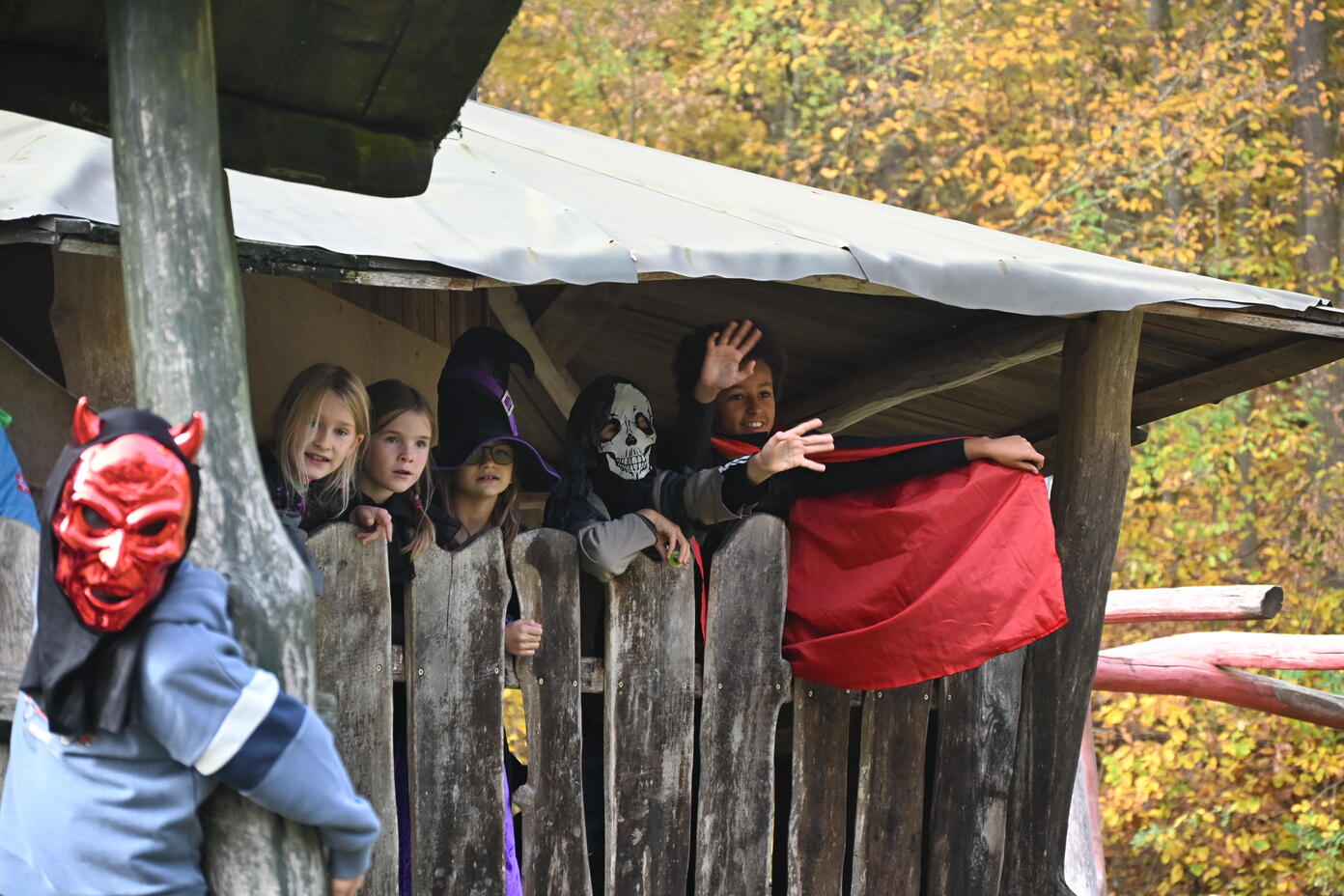 Kinder in Halloween Kostuemen winken froehlich aus einer Holzhuette im Wald