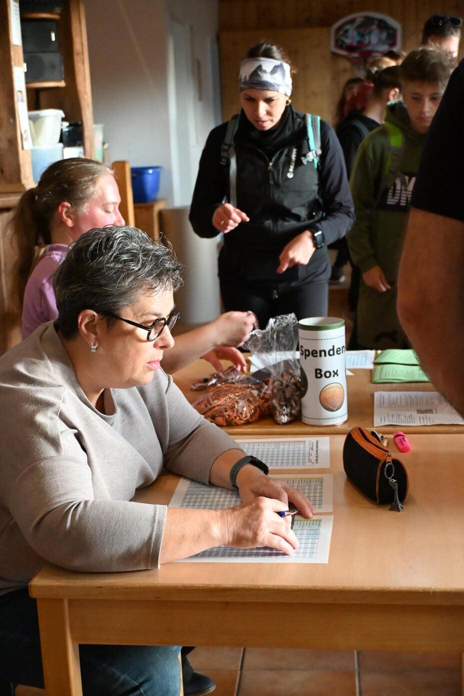 Eine Frau mit Brille zeigt konzentriert auf eine Liste neben einer Spendenbox