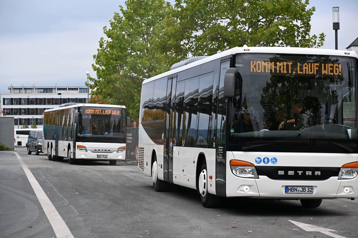 Zwei weisse Setra Busse mit der Anzeige Komm mit lauf weg auf einem Parkplatz