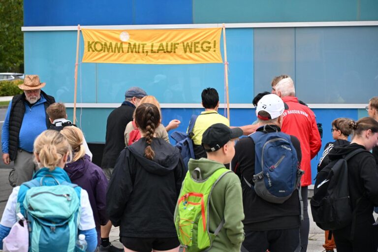 Menschengruppe mit Rucksaecken vor gelbem Banner Komm mit lauf weg
