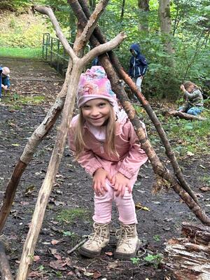 Laechelndes Maedchen in rosa Kleidung hockt unter einem Aesttipi im Wald