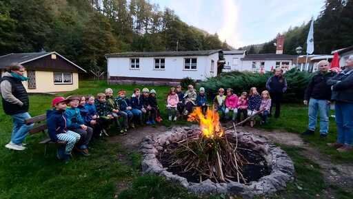 Eine Gruppe Kinder und Erwachsene sitzt um ein Lagerfeuer im Freien