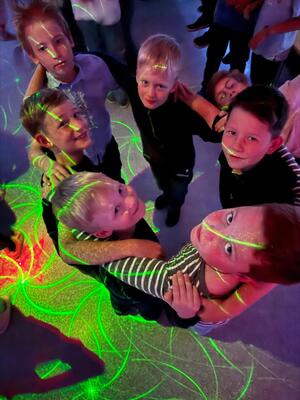 Laechelnde Kinder im gruenen Laserlicht blicken nach oben in die Kamera