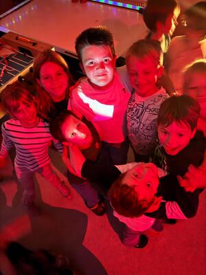 Eine Gruppe laechelnder Kinder blickt im farbigen Discolicht nach oben