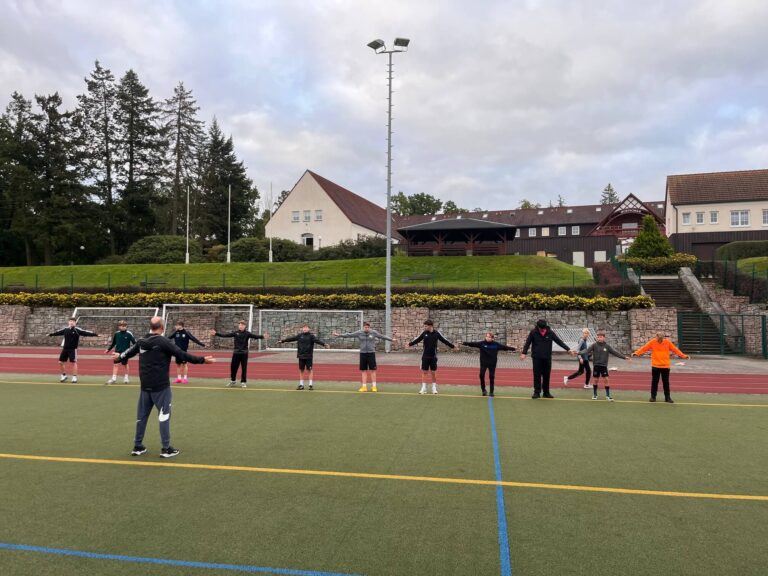 Ein Trainer leitet eine Gruppe Jugendlicher beim Aufwaermen auf dem Sportplatz an