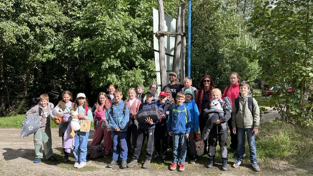 Eine laechelnde Gruppe von Kindern und Erwachsenen vor gruenen Baeumen